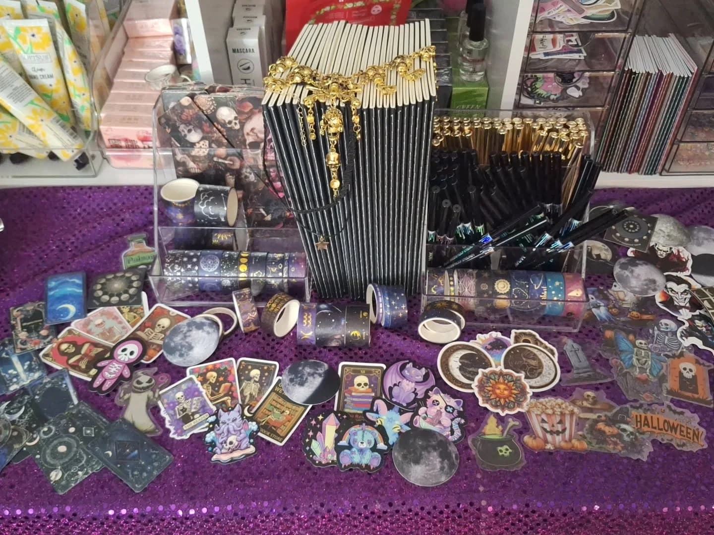 Spooky notepads, black and gold pens, moon stickers, and decorative tape on purple sequins